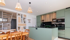 A modern kitchen with a central island, wooden dining table, and chairs. - Maison Desmathi: terrace with jacuzzi, garden, in Saint-Pierre-Quiberon (Saint-Pierre-Quiberon)