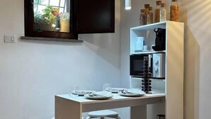 A modern kitchen with a dining area, a TV mounted above the window, and a white cabinet with jars. - The Little House on Sannio Street (Roma)