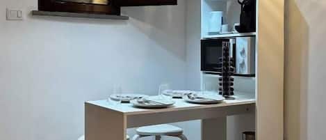 A modern kitchen with a dining area, a TV mounted above the window, and a white cabinet with jars.