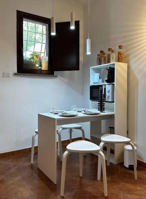 Una cocina moderna con zona de comedor, un televisor sobre la ventana y un armario blanco con frascos.