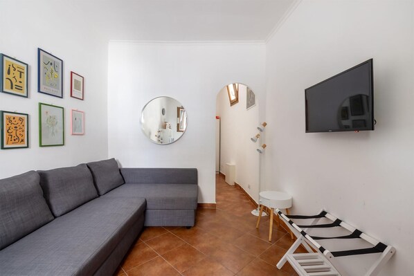 A modern living room with a grey sofa, a round mirror, a flat-screen TV, and a white side table. - The Little House on Sannio Street (Roma)