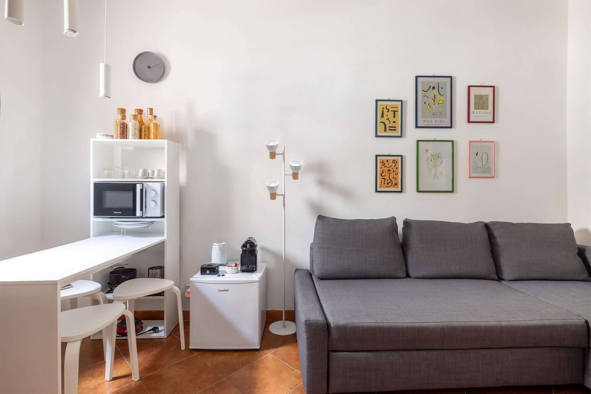 En moderne opholdsstue med et hvidt tekøkken, en grå sofa og billedkunst på væggen.