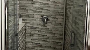 A shower with a stone wall, a handheld showerhead, and a glass door. - The Little House on Sannio Street (Roma)