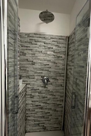 Ducha con pared de piedra, cabezal de ducha de mano y puerta de cristal.