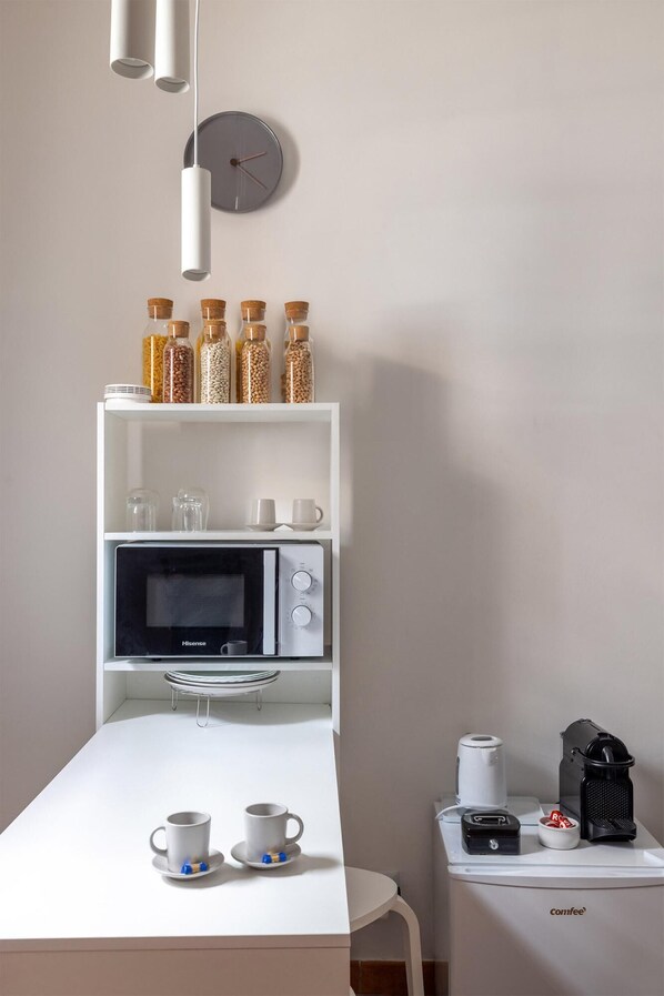 Una kitchenette con microondas, cafetera y estantes para guardar objetos.