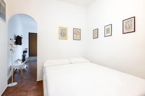 Ein Hotelzimmer mit einem Bett, einem Schreibtisch und einem Stuhl. Vier gerahmte Kunstwerke sind an der Wand angebracht.