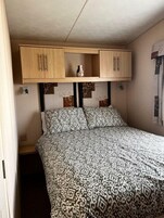 Un dormitorio con una colcha estampada, dos almohadas, un jarrón en un estante sobre la cama y un cabecero con un diseño geométrico.