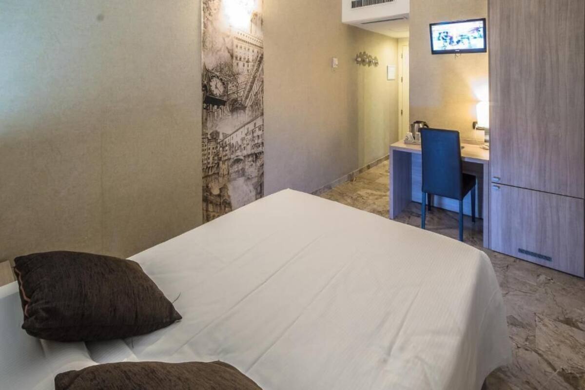 Una camera d'albergo con un letto, una scrivania con sedia, una televisione e un frigorifero.