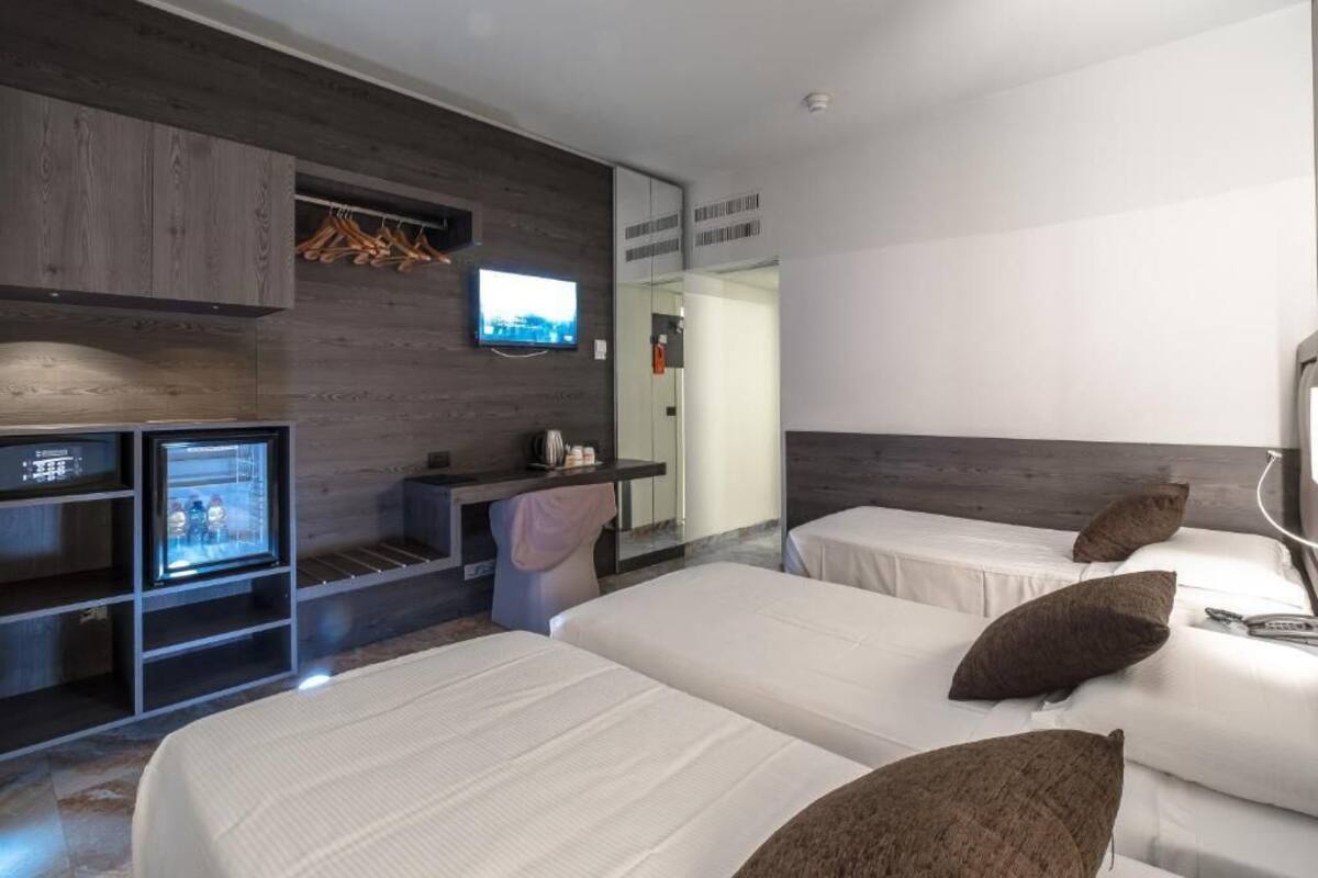 Camera d'albergo moderna con due letti, una TV, una scrivania e uno specchio.