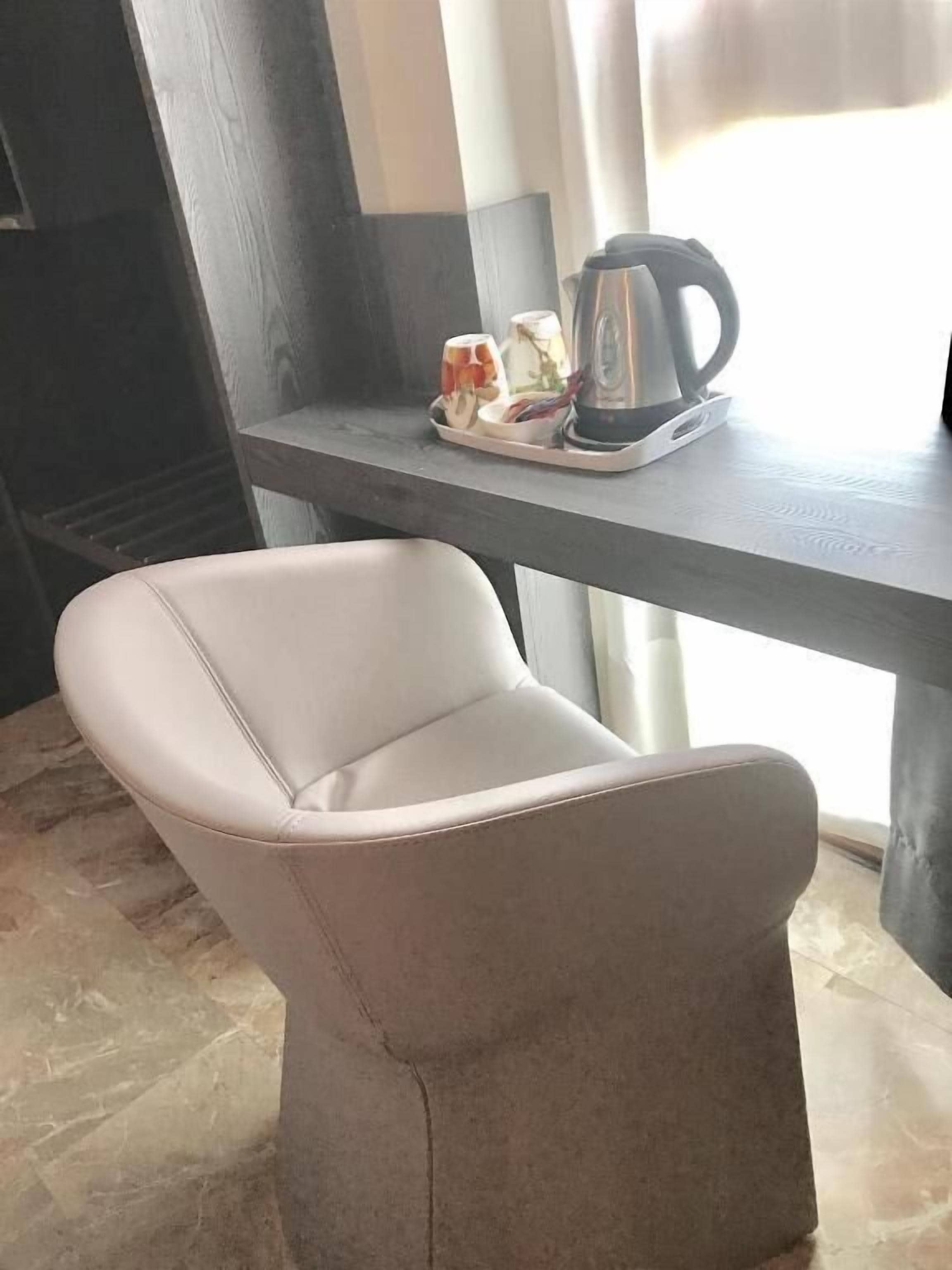 A modern kitchen with a sleek black countertop, a white chair, and a kettle on the table.