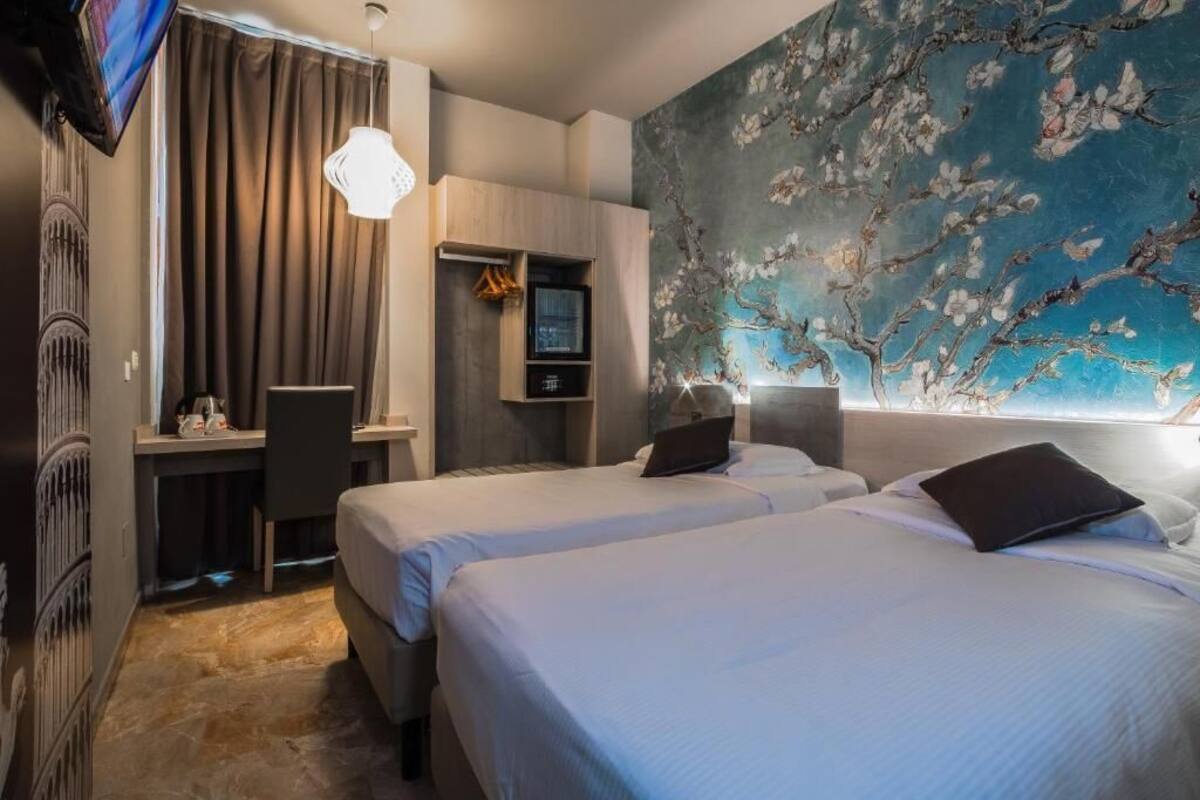 Una camera d'albergo con due letti, una scrivania, una TV e un grande affresco floreale sulla parete.