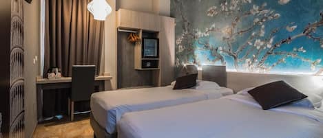 A hotel room with two beds, a desk, a TV, and a large floral mural on the wall.