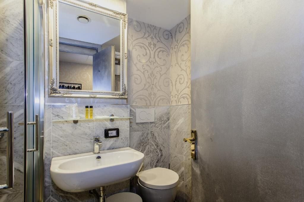 Un baño con lavamanos de mármol, inodoro y un espejo grande.