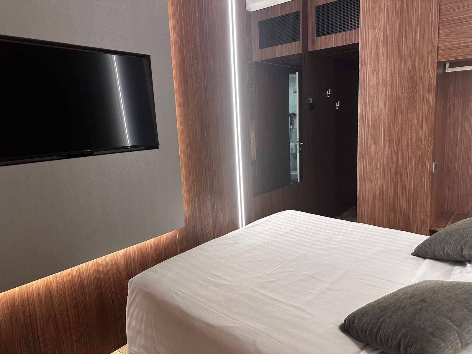 Ein modernes Hotelzimmer mit einem Bett, einem an der Wand befestigten Flachbildfernseher und Holzvertäfelung.