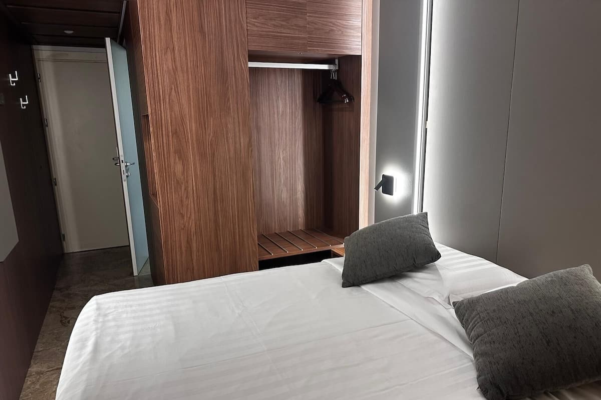 Una camera da letto con un letto, cuscini, un armadio e una lampada a sospensione.
