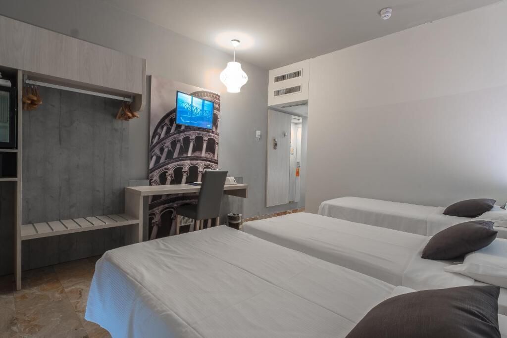 A hotel room with two beds, a desk, a chair, a television, and a wardrobe.