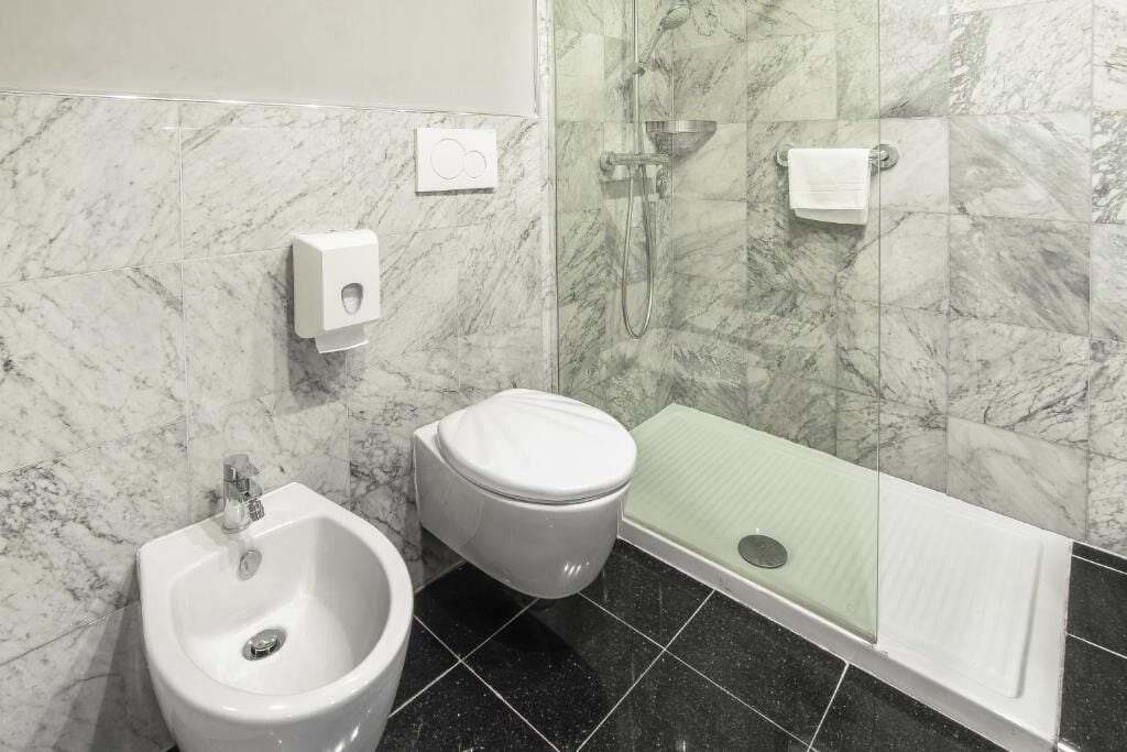Un baño con bidé, inodoro y ducha con mampara de vidrio.