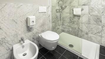 Un baño con bidé, inodoro y ducha con mampara de vidrio.