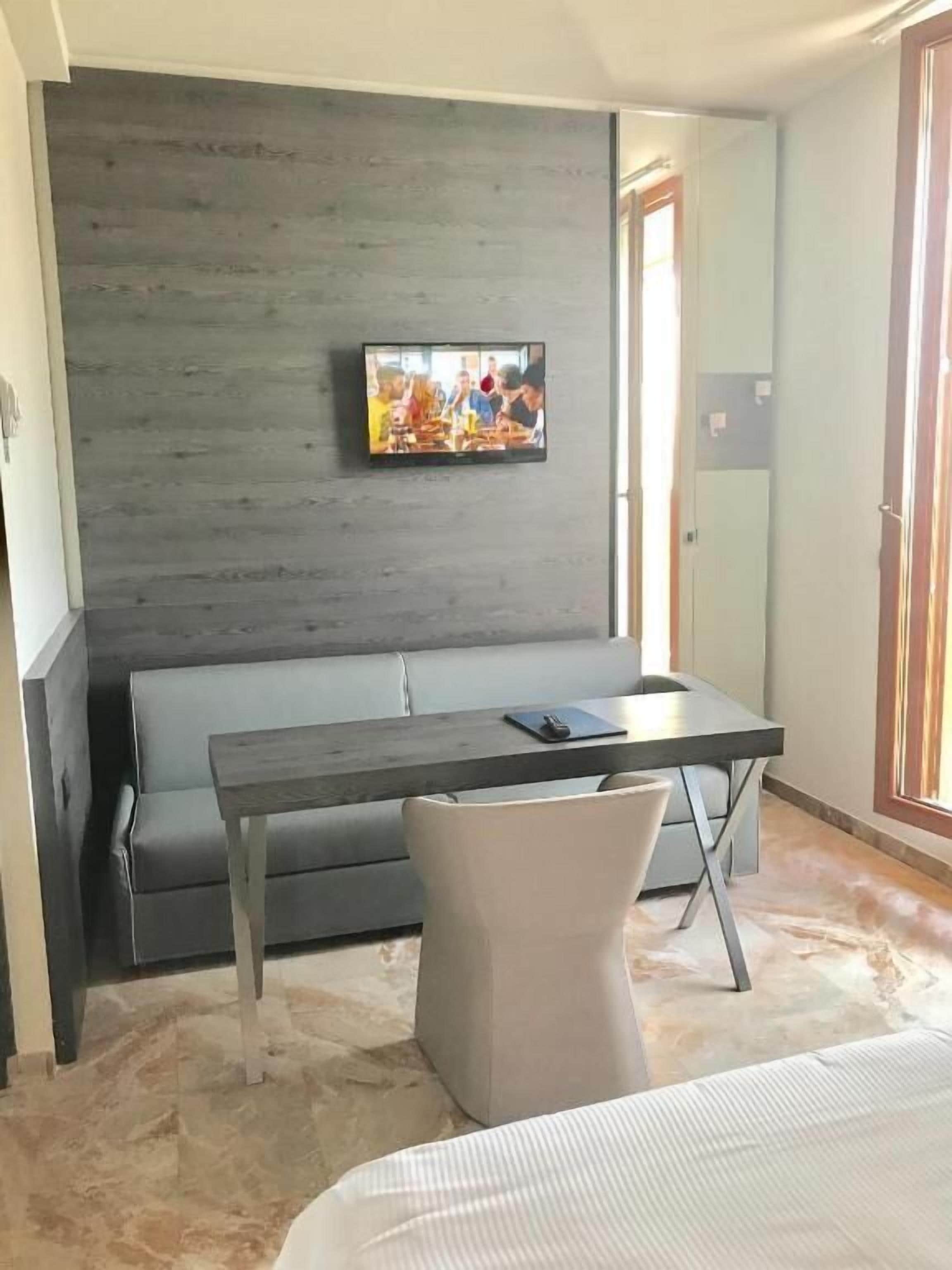 Una habitación moderna con un sofá gris, una mesita pequeña y un televisor fijado a una pared de madera.