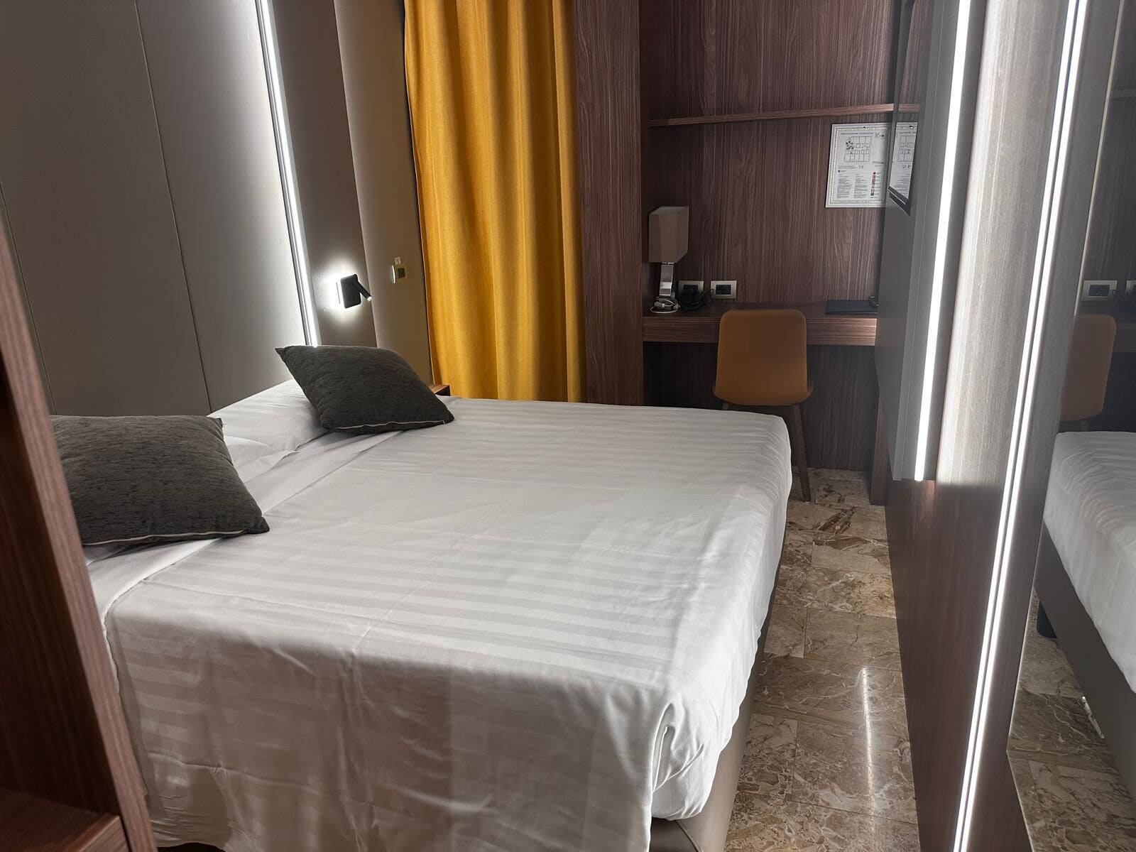 A hotel room with a bed, a desk, a chair, and a curtain.