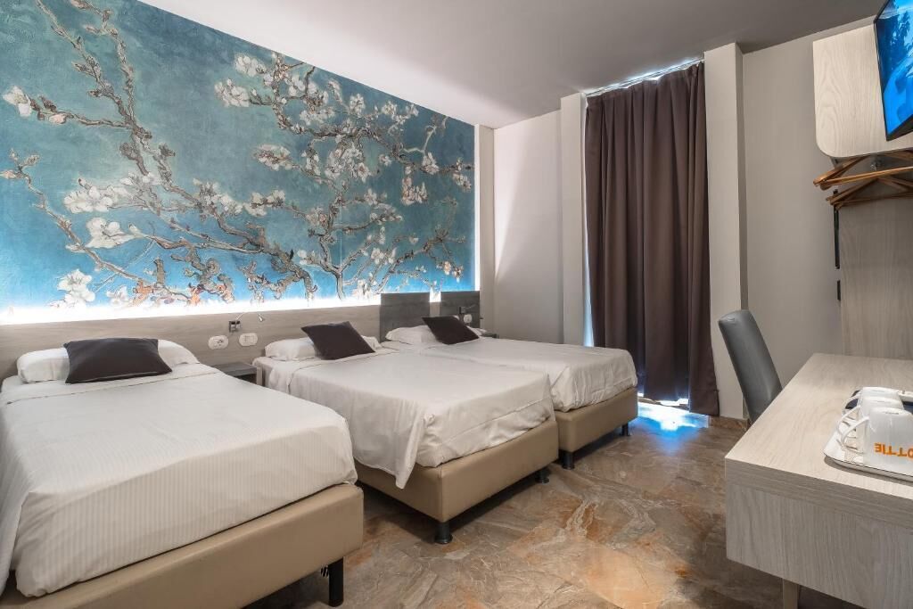 A hotel room with two beds, a large floral mural on the wall, a desk with a coffee machine, and a TV mounted on the wall.