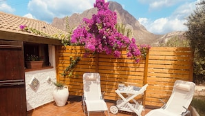 A patio with two white lounge chairs, a small table, and a potted plant.