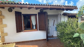 A building with a tiled patio, a window with wooden shutters, and a door leading inside.