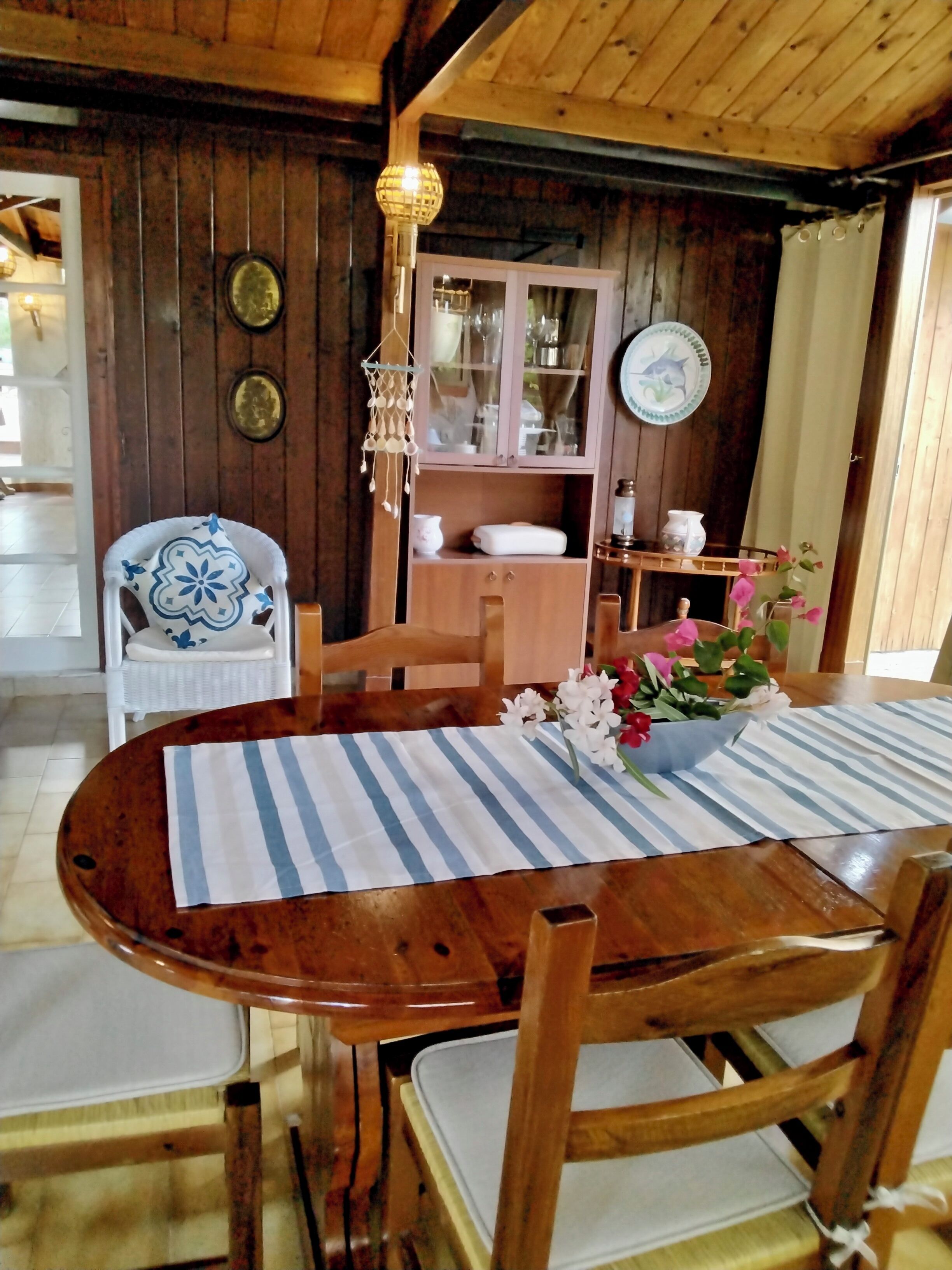 A wooden dining table with striped placemats, surrounded by wooden chairs. A decorative hanging light fixture is above the table.