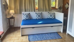 A bedroom with a bed, a bedside table with a lamp, a window with curtains, and a radiator.