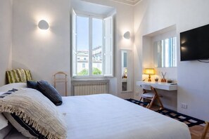 A bedroom with a bed, a desk with a chair, a television, and a window with a view of buildings. - LVD Lucina Luxury Apartament al Centro di Roma (Rome)