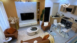 Un soggiorno moderno con divano, tavolino e televisore, adiacente a una cucina con lavatrice.