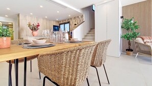Zona de menjador moderna amb taula de fusta, cadires de vimetla i una escala que condueix a un pis superior.