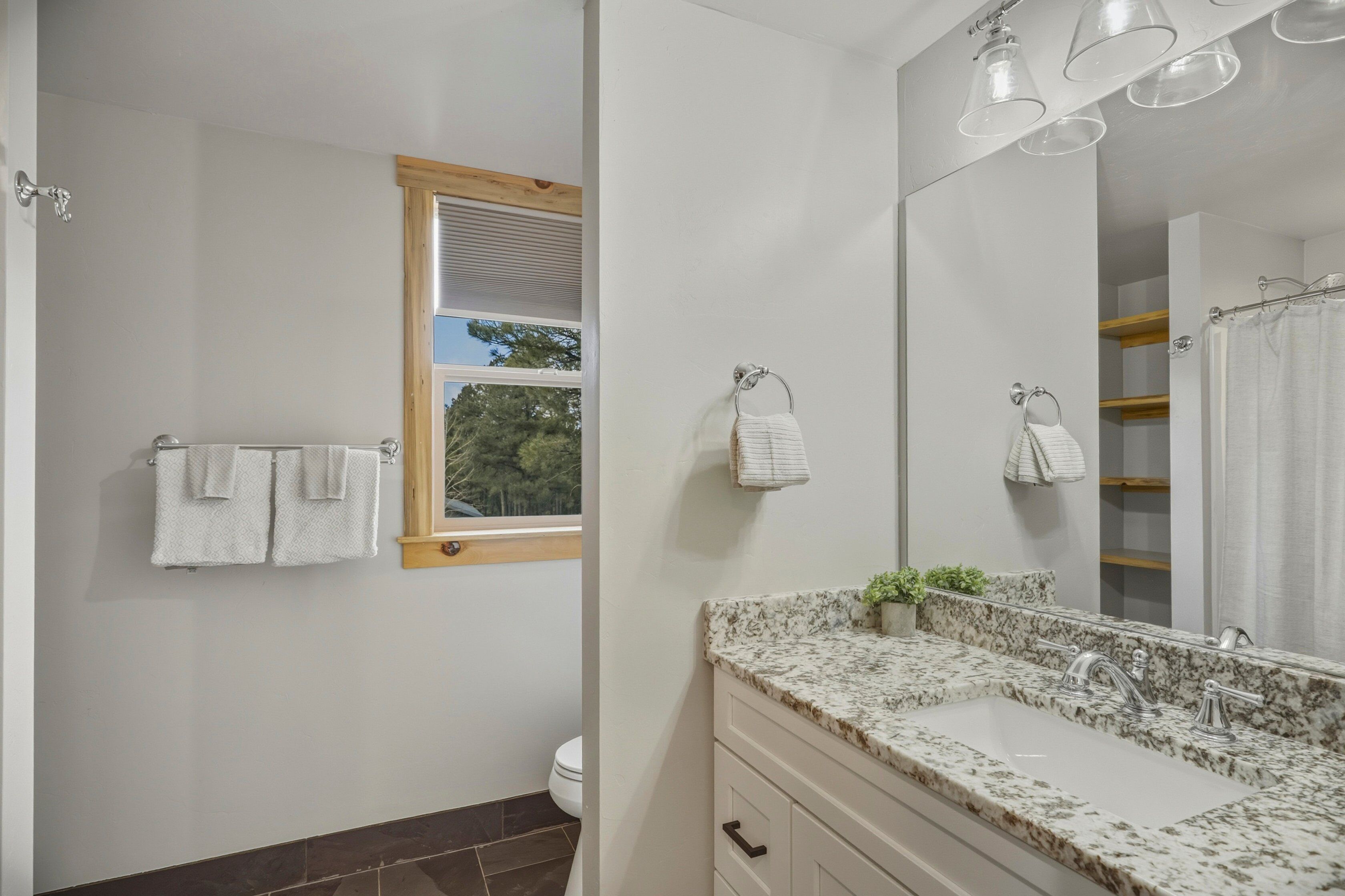 Une salle de bain avec un lavabo en marbre, un grand miroir et une fenêtre avec des stores.