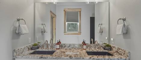 Un baño con dos lavamanos, un espejo grande y ganchos para toallas.