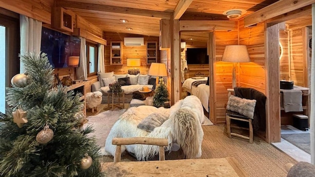 Ein gemütliches Blockhaus-Interieur mit Kamin, einer Sofagarnitur, einem Weihnachtsbaum und einem Essbereich.