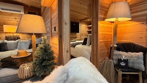Ein gemütliches Blockhaus-Interieur mit einer Couch, zwei Lampen, einer kleinen Weihnachtstanne und einem Sessel mit Kissen.