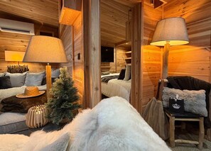 A cozy log cabin interior with a sofa, two lamps, a small Christmas tree, and a chair with a cushion. - Le Chalet du lac (Biscarrosse)