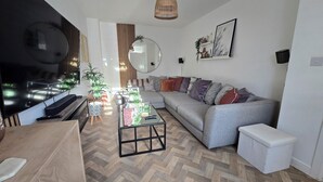 Moderni olohuone, jossa on harmaa sohva, sohvapöytä, televisio ja kalanruotokuviollinen lattia.