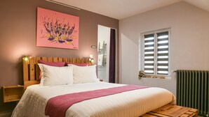 Ein Schlafzimmer mit einem hölzernen Bett, einem floralen Bild mit rosa Blumen, einem Fenster mit Fensterläden und einer Heizung.