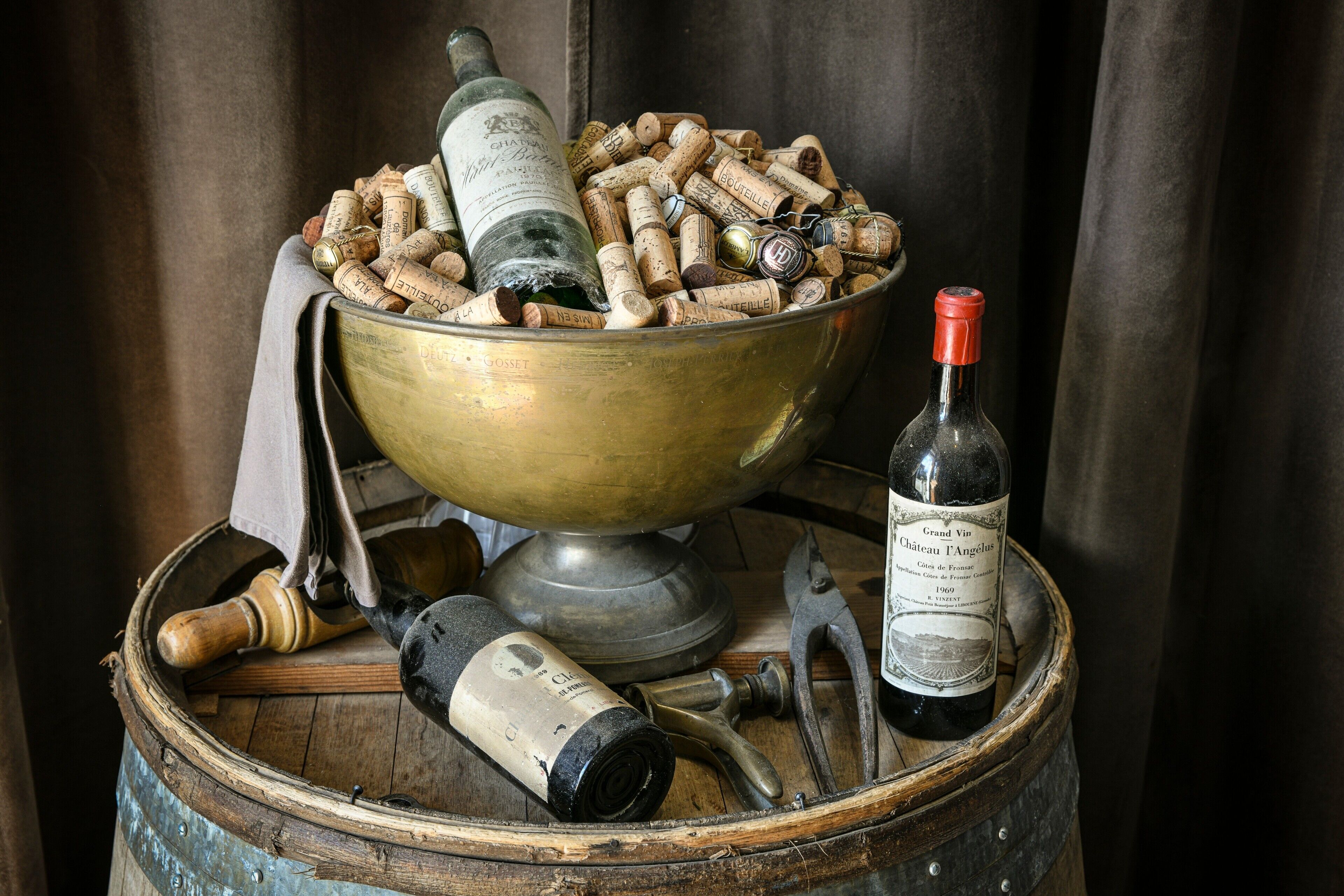 Een bronzen kom gevuld met wijnkurken, een fles Grand Vin Chateauneuf, en een houten vat met een fles en een kurkentrekker.
