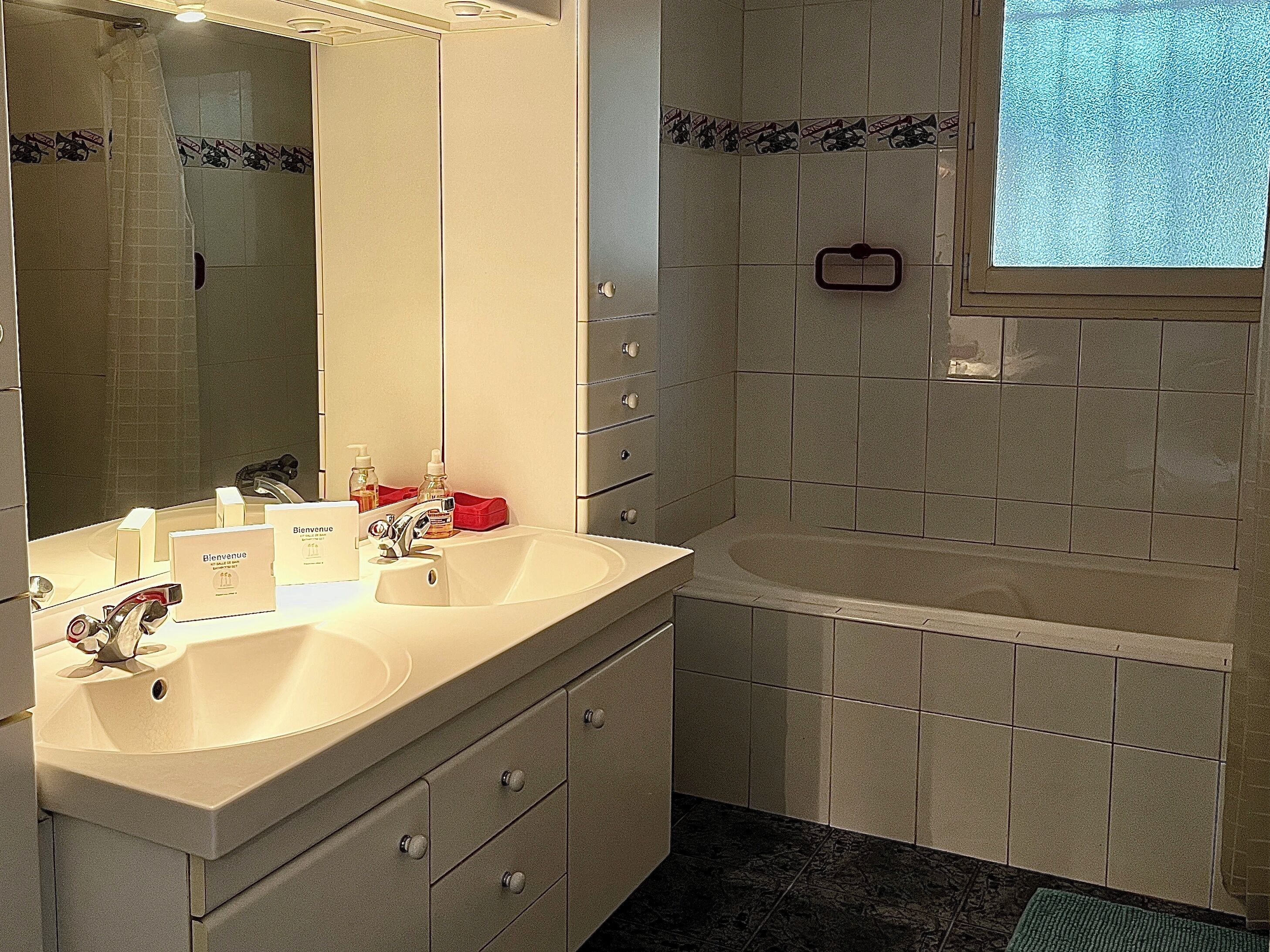 Une salle de bain avec un double lavabo, un miroir, un porte-serviettes et un espace douche.