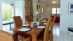A dining area with a wooden table set for six, surrounded by wicker chairs. There is a view of a kitchen in the background. - CAP DE HE' MAIN HOUSE (Lit-et-Mixe)