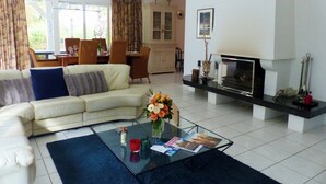 A living room with a sofa, coffee table, fireplace, and dining area. - CAP DE HE' MAIN HOUSE (Lit-et-Mixe)