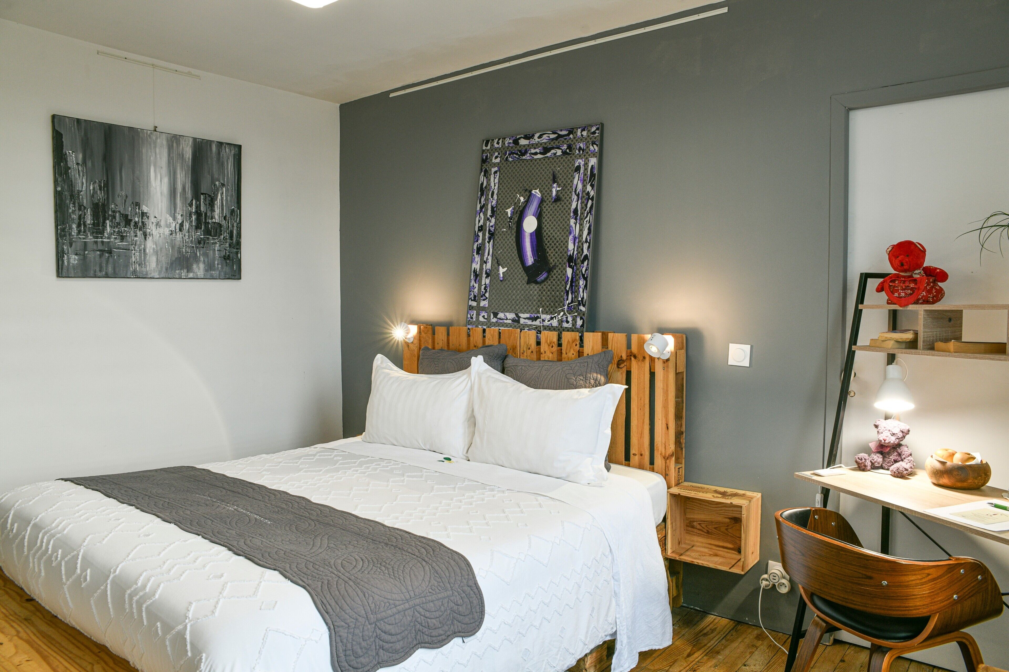 A bedroom with a bed, a desk, a chair, and a wall-mounted shelf.