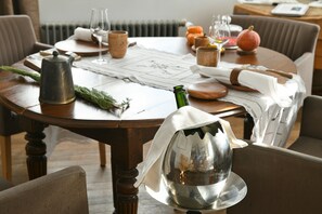 Une table de salle à manger ronde, surmontée d’un récipient en métal, avec une bouteille verte et un tissu blanc.
