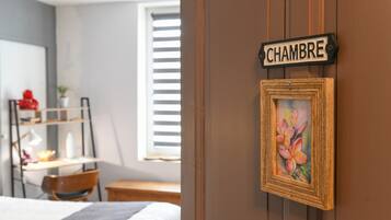 A bedroom with a bed, a desk, a chair, a window with blinds, a door with a sign, and a framed picture.