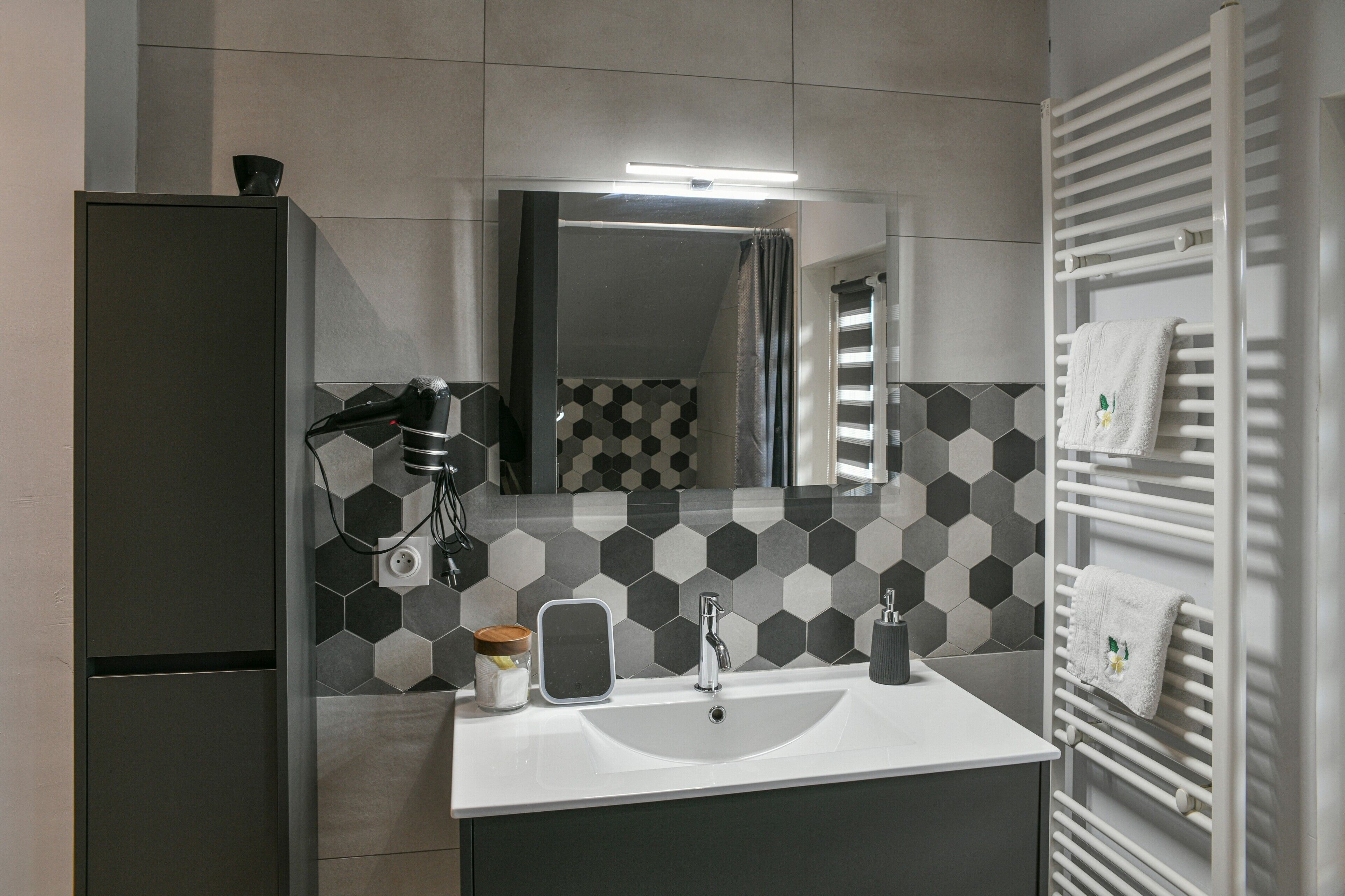 Een moderne badkamer met een wit wastafelmeubel, een spiegel, een handdoekhouder en een achterwand van hexagontegels.