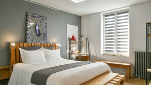 Een slaapkamer met een houten bed, een bankje, een radiator en een raam met zonwering.