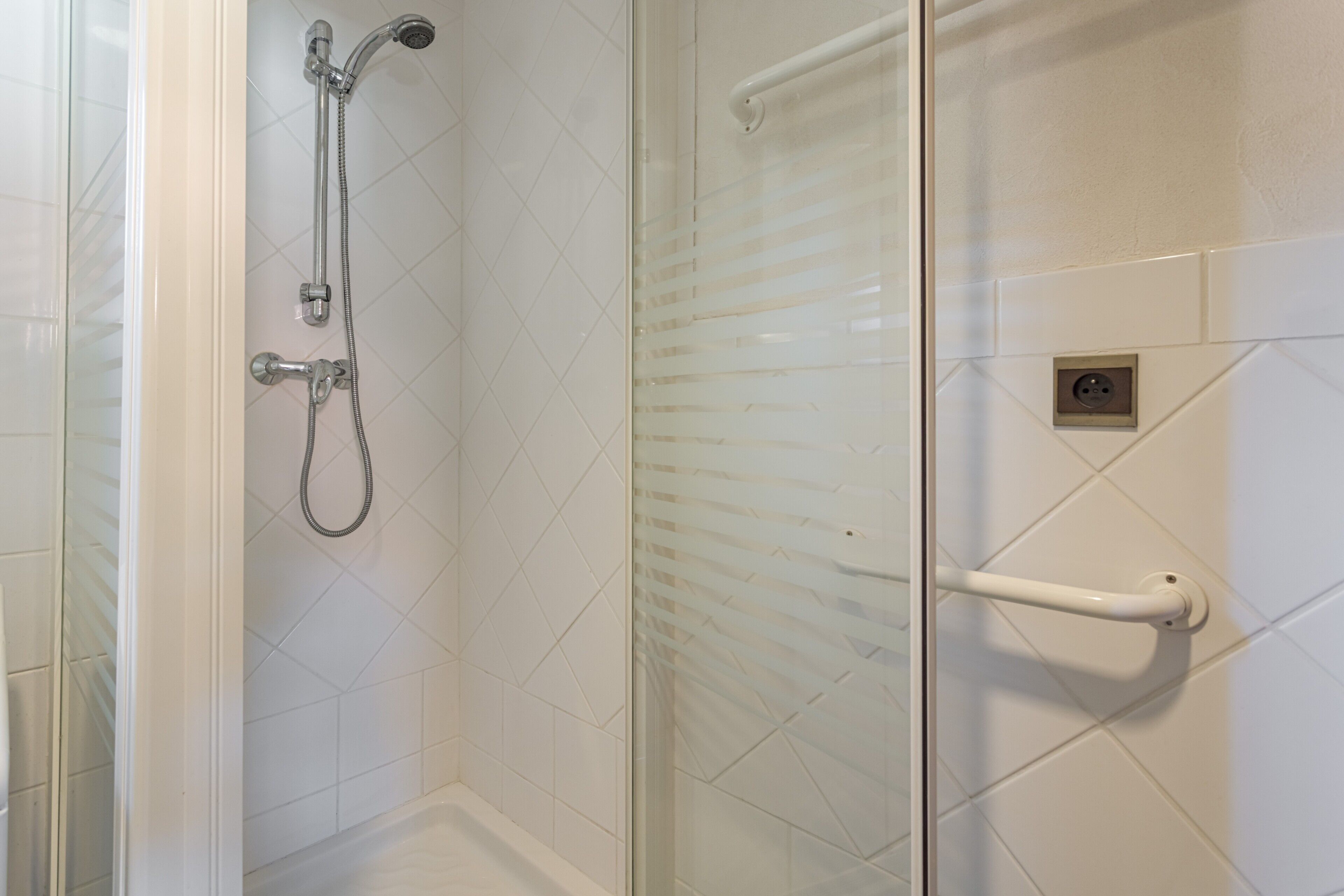 A shower with a glass door, a handheld showerhead, and a wall-mounted handrail.