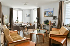 Una sala de estar con sofás de cuero, una mesa de centro de vidrio, una zona de comedor con sillas, un área de cocina con barra y un cuadro en la pared.